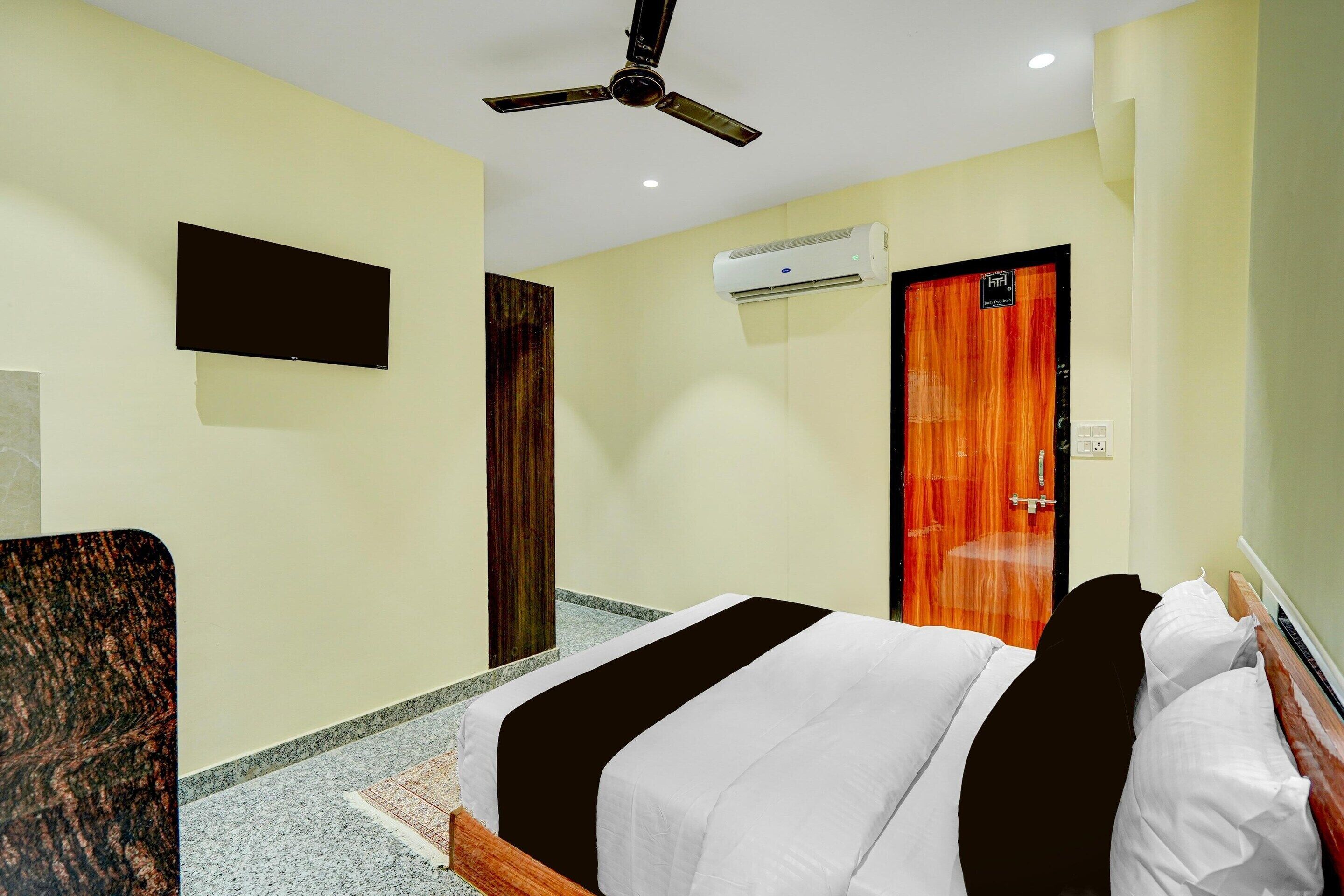 Une chambre d’hôtel équipée d’un lit, d’un ventilateur de plafond, d’un climatiseur et d’un téléviseur fixé au mur.