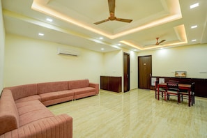 A modern room with a sectional sofa, a dining area with wooden chairs, and ceiling fans. - Palette Hotel & Resorts Riico (Jaipur)