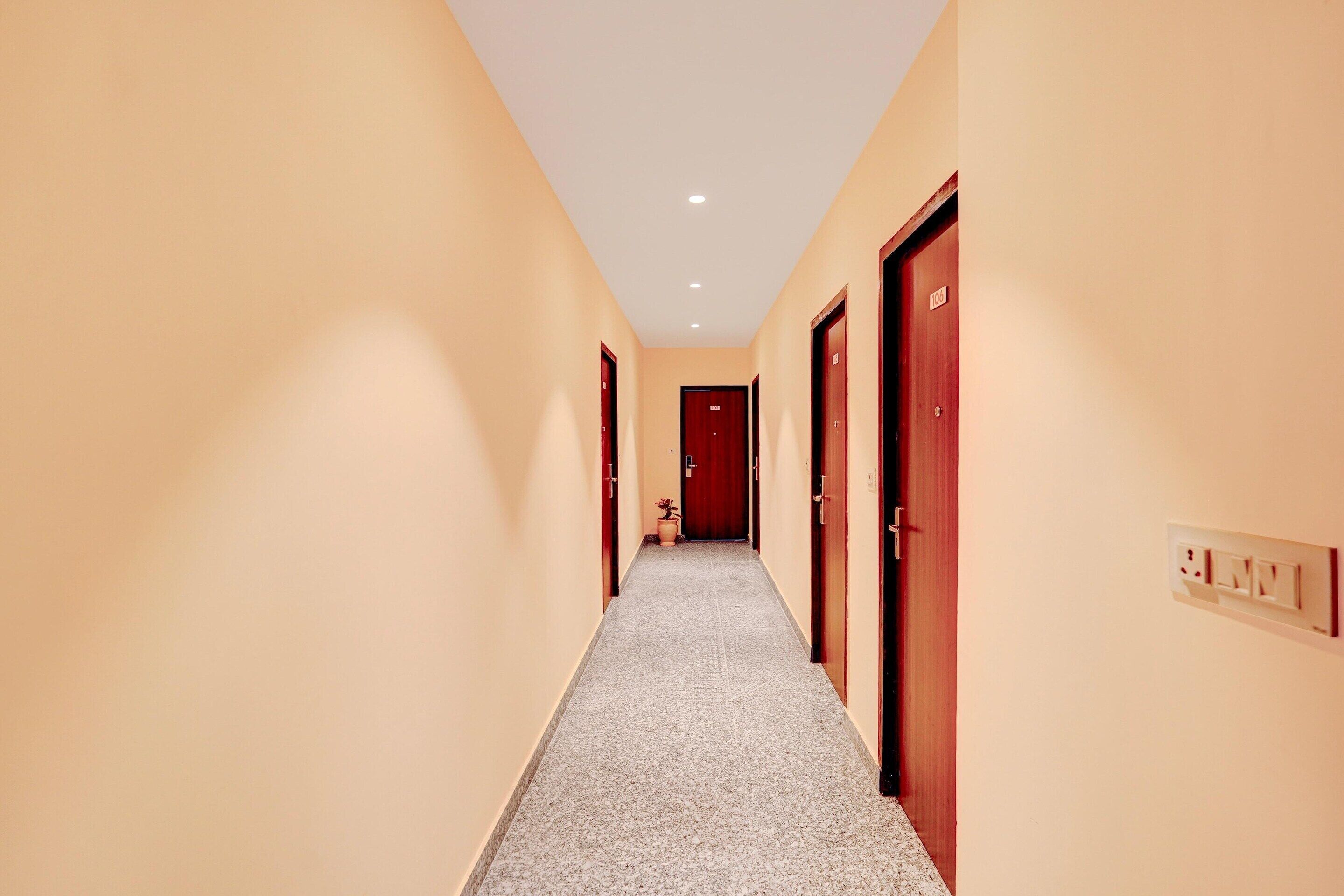 A hotel hallway with carpeted floors, wooden doors, and a light switch on the wall.