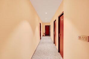 A hotel hallway with carpeted floors, wooden doors, and a light switch on the wall. - Palette Hotel & Resorts Riico (Jaipur)