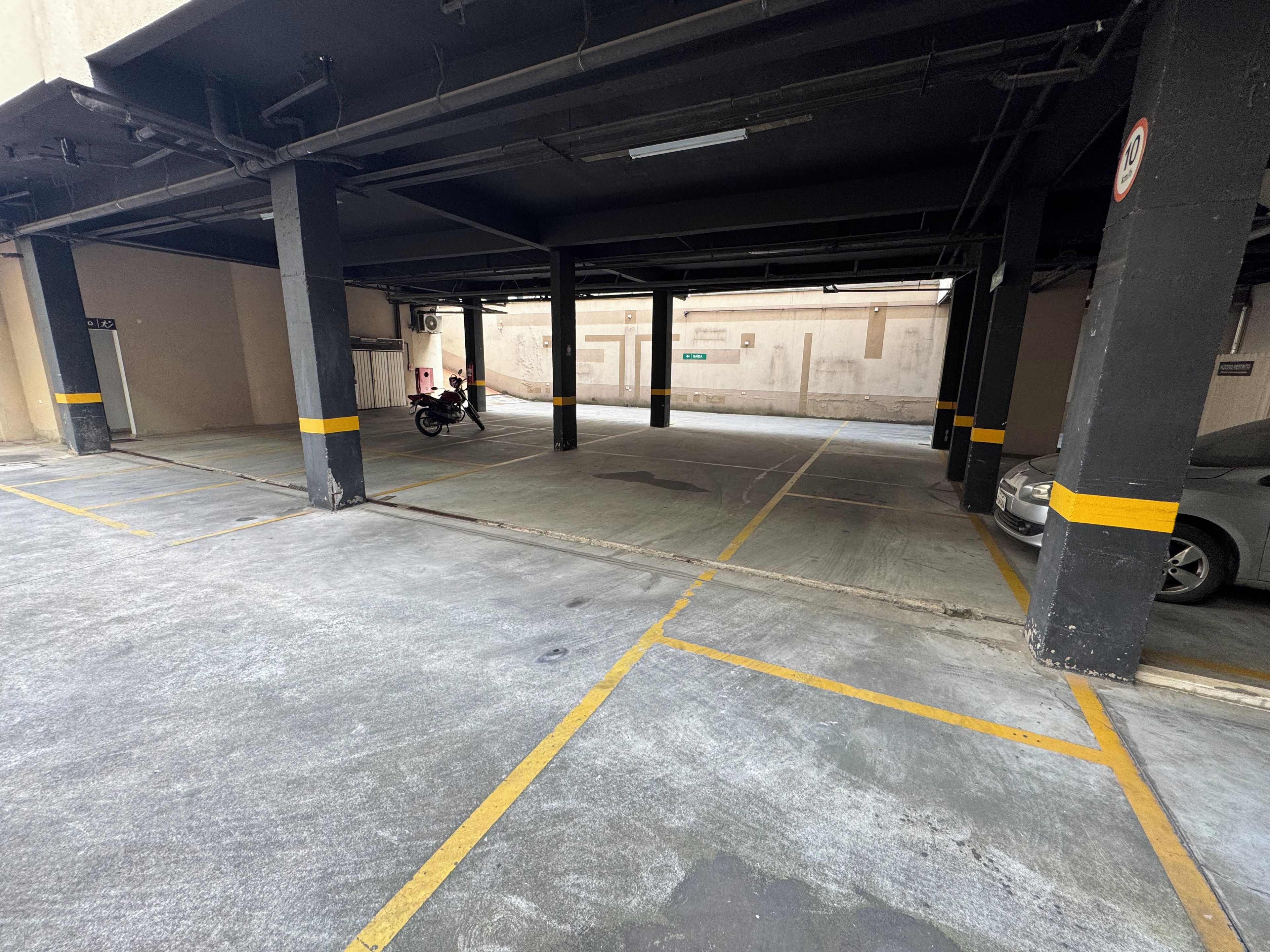 A parking garage with concrete floors, yellow lines, and black pillars with yellow stripes.
