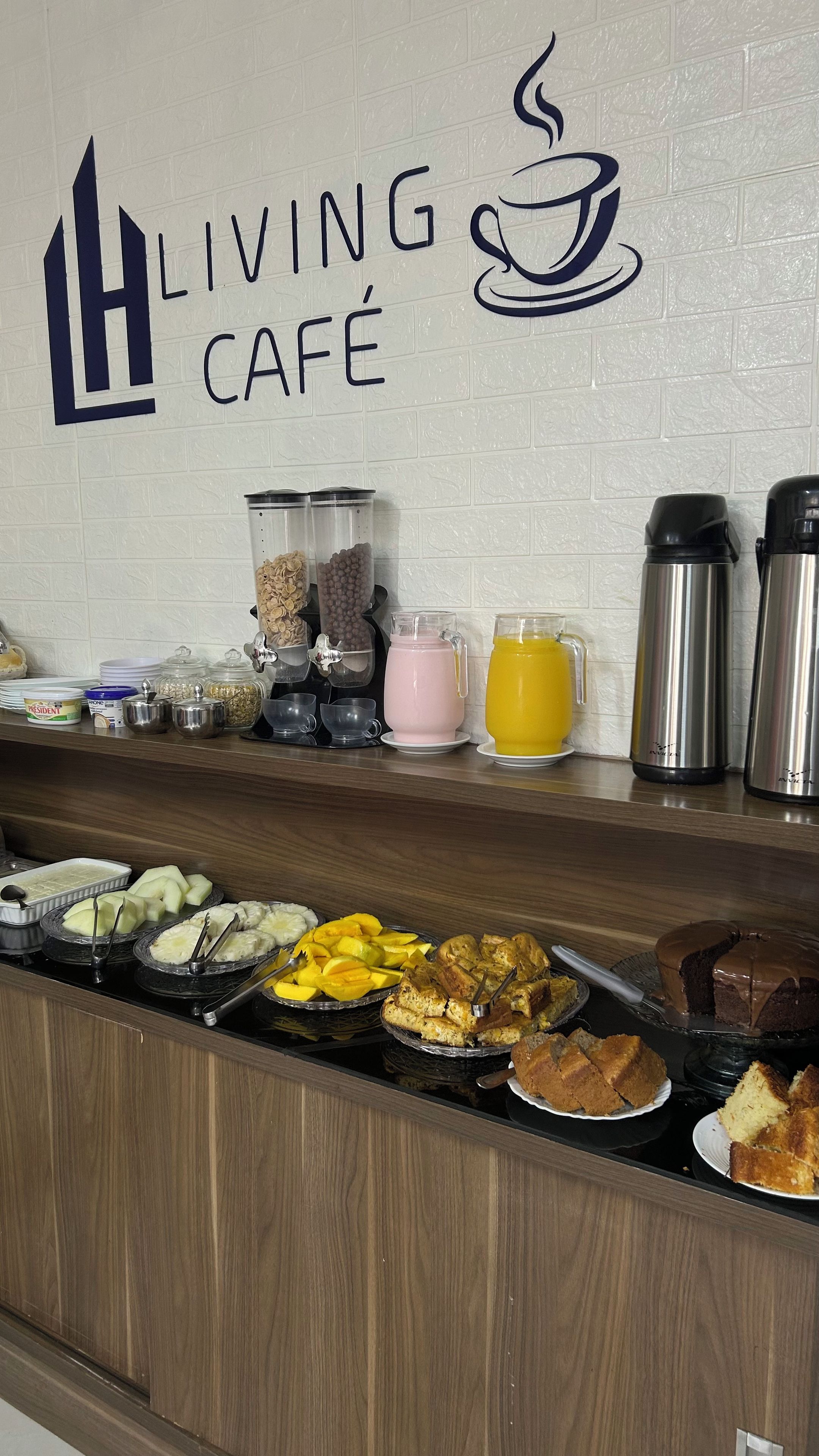 Espaço de buffet de café da manhã com um letreiro que diz 'Living Café' e diversas opções de comida e bebida.