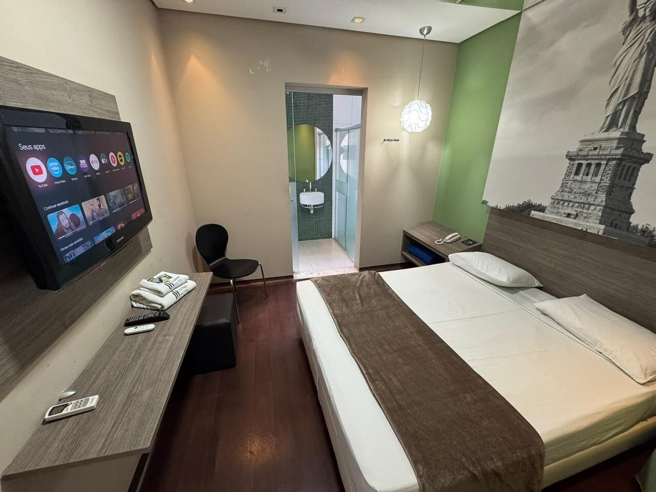 Habitación de hotel con cama, escritorio con televisor, silla y baño visible a través de una puerta abierta.