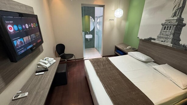 A hotel room with a bed, a desk with a TV, a chair, and a bathroom visible through an open door. - Add Hotéis Center Norte (São Paulo)