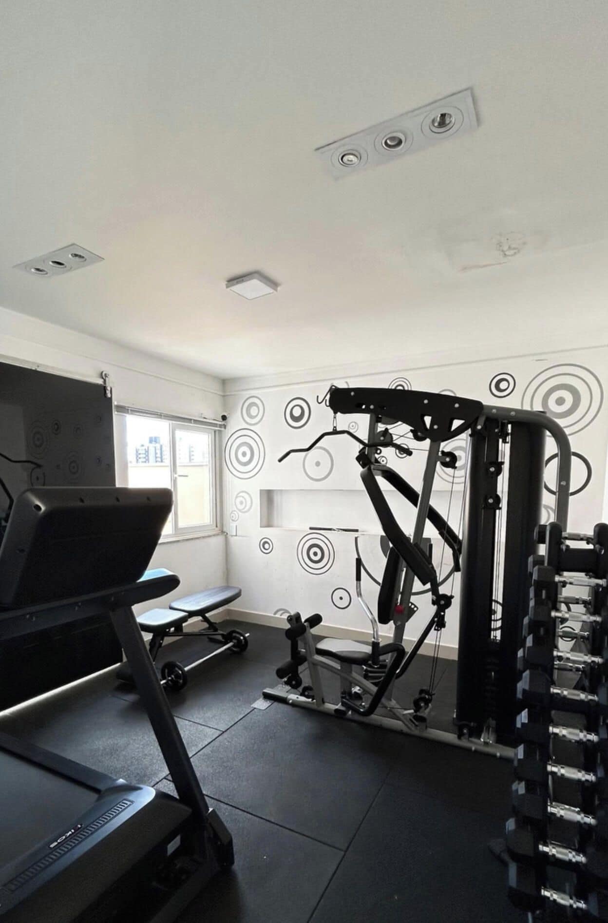 Une salle de sport équipée de matériel d’exercice, d’un tapis de course et d’un mur orné de motifs circulaires.