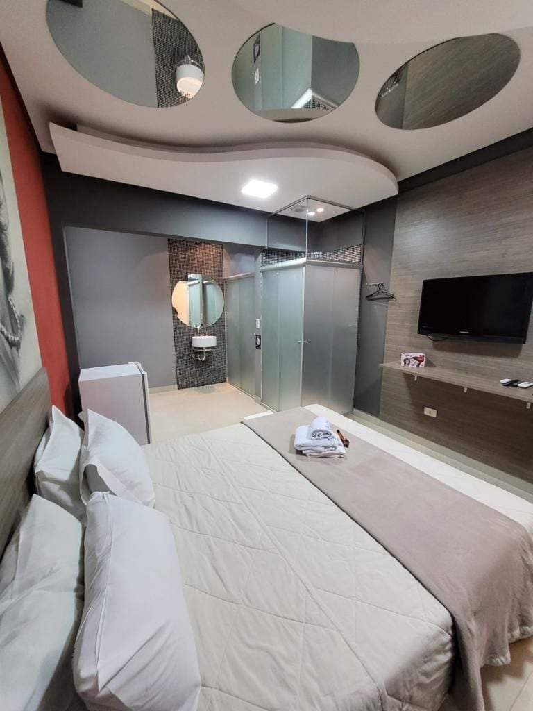 A modern hotel room with a bed, a TV, a mirror, and a wardrobe.