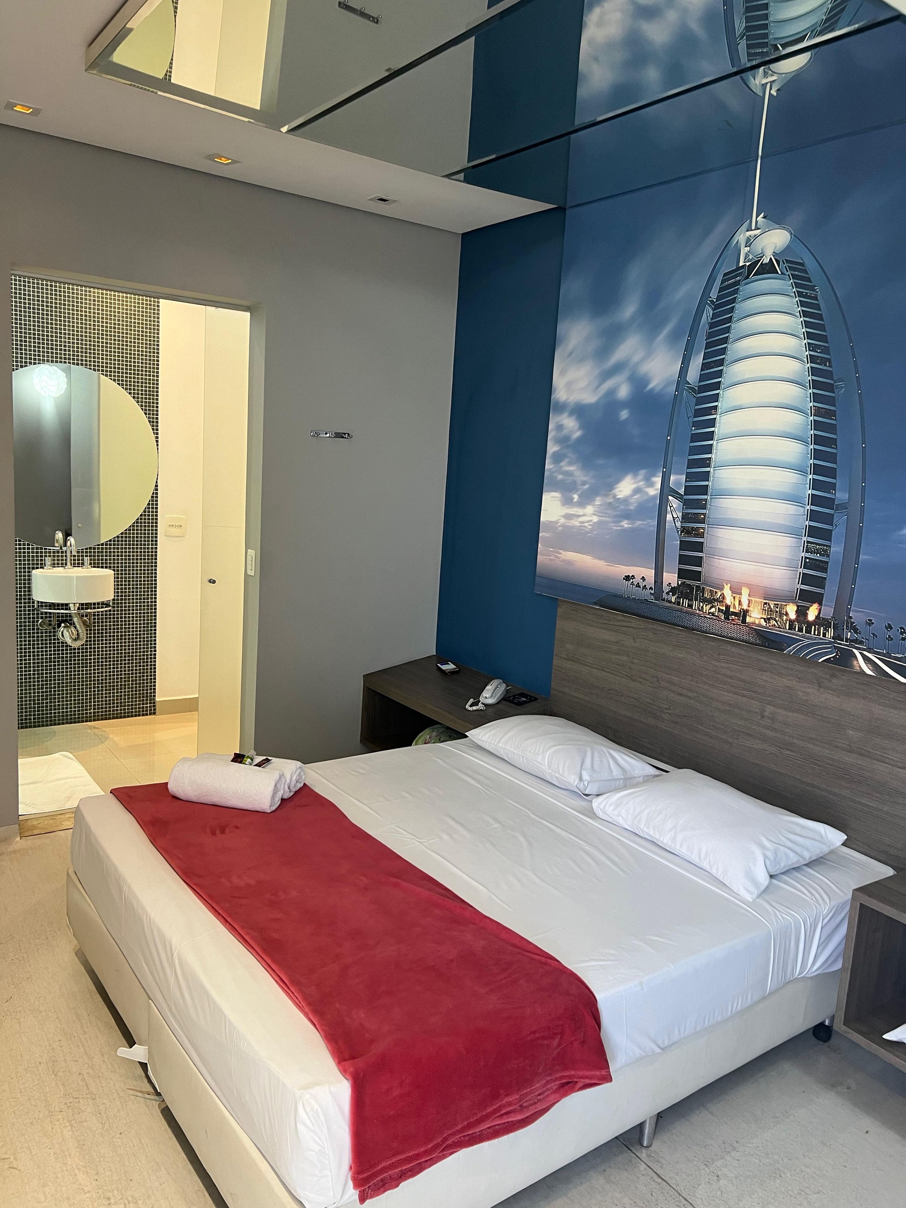 A modern hotel room with a bed, a nightstand, a mirror, and a large window.