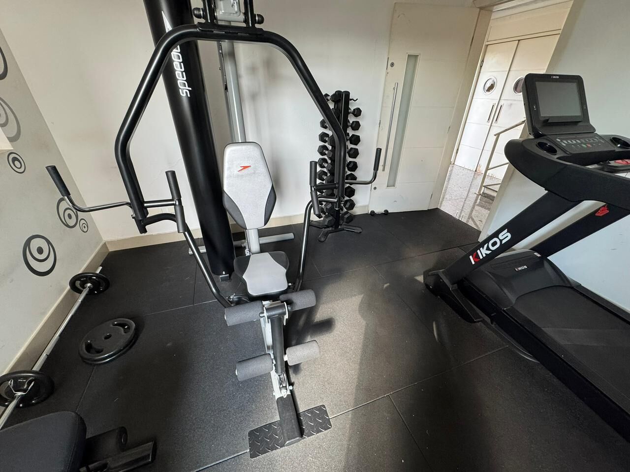 Un gimnasio con una banca de pesas, una jaula para sentadillas y una cinta de correr.