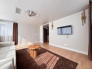 A modern living room with a sofa, a round coffee table, a flat-screen TV mounted on the wall, and a wooden floor. - Modern 1BR Residence Near Galataport (Istanbul)