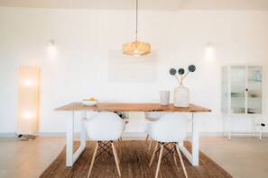 Un comedor moderno con una mesa de madera, sillas blancas, una lámpara colgante y un jarrón con adornos esféricos.