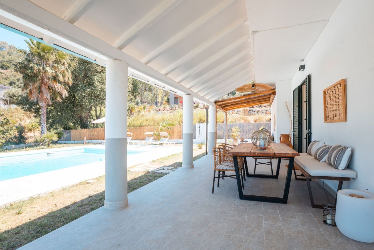 Un patio exterior con piscina, una mesa de madera y sillas.