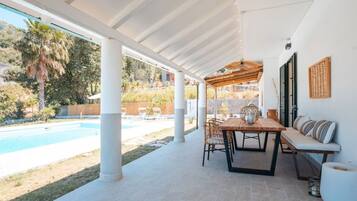 Un patio exterior con piscina, una mesa de madera y sillas.