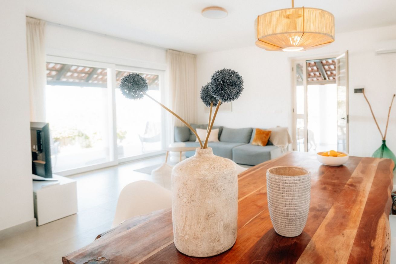 A modern living room with a wooden coffee table, a textured vase, and a hanging light fixture.