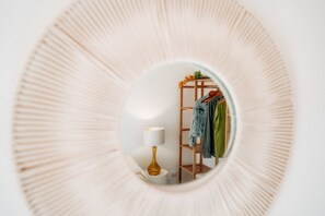 A circular mirror reflecting a room with a wooden shelf, a lamp, and hanging clothes.