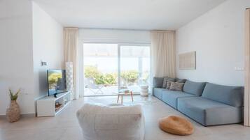En moderne stue med sofa, skammel og fjernsyn på et hvidt møbel.