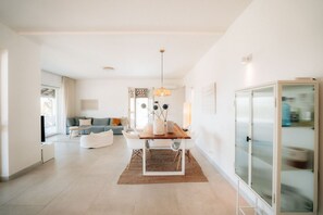 Un salón espacioso con una mesa de comedor de madera, sofás blancos y una vitrina de vidrio.