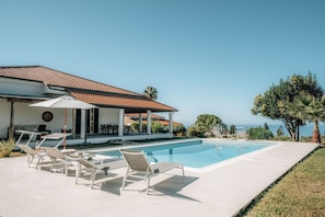 A swimming pool with lounge chairs, a patio area, and a view of the ocean.