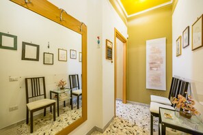 A hallway with framed pictures, a mirror, a wooden chair, a glass table with a vase, and a door leading to another room. - Colli Aminei Vista Golfo (Naples)