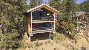 Une cabane en bois à deux étages, dotée d’un balcon et entourée d’une forêt dense.