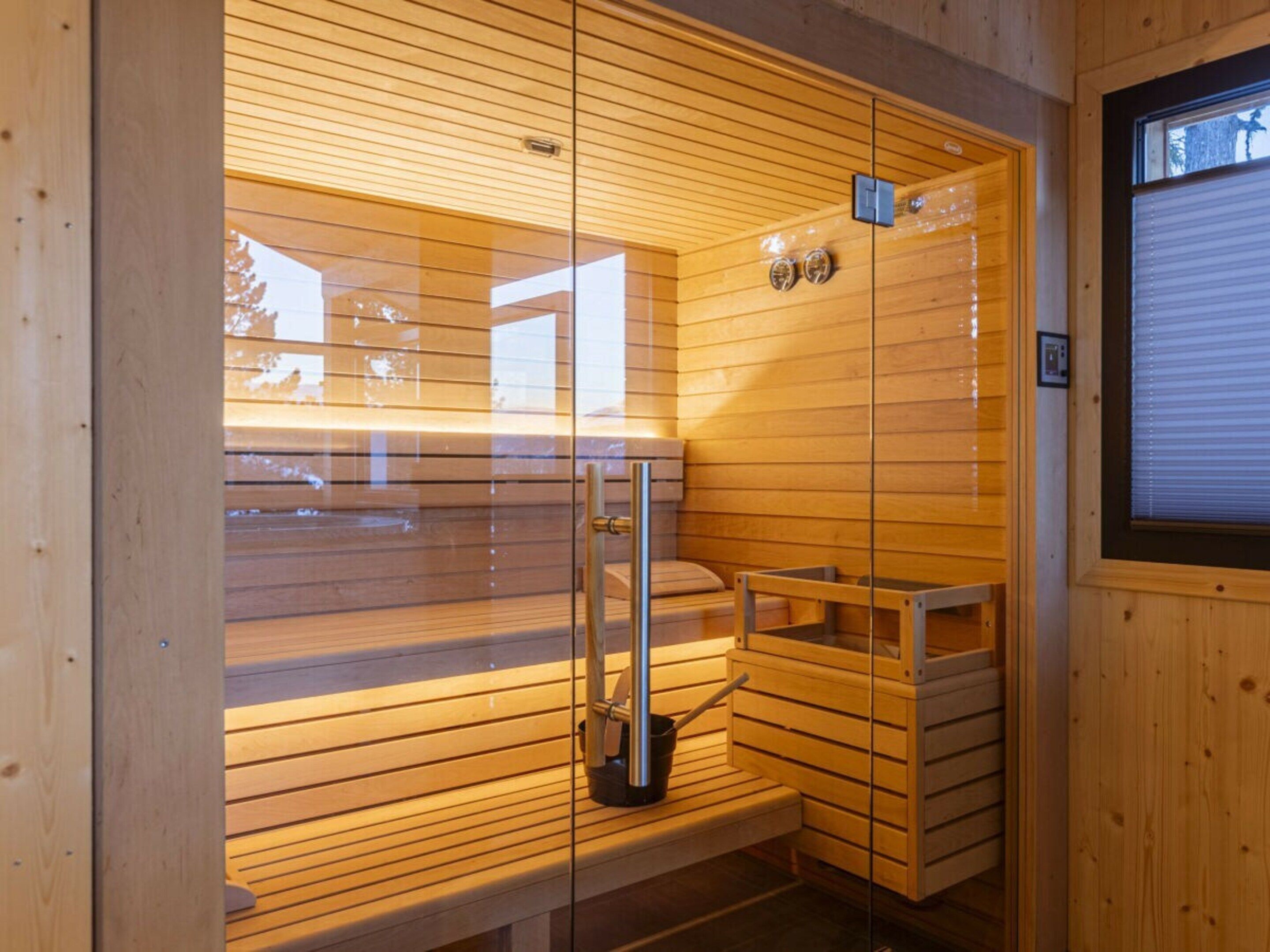 A sauna with wooden slats, a glass door, and a bench.