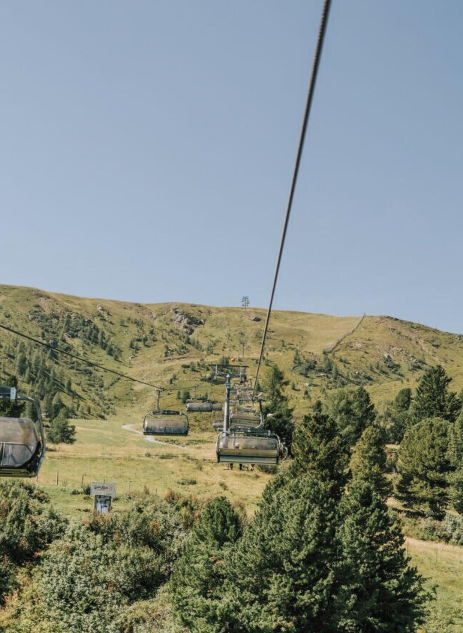 A cable car system in a mountainous area with greenery and clear skies.