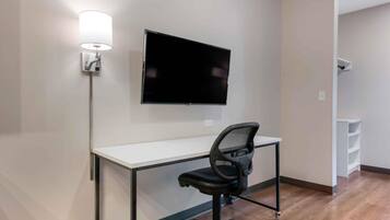 A modern office space with a white desk, black office chair, mounted flat-screen TV, and a wall-mounted lamp.