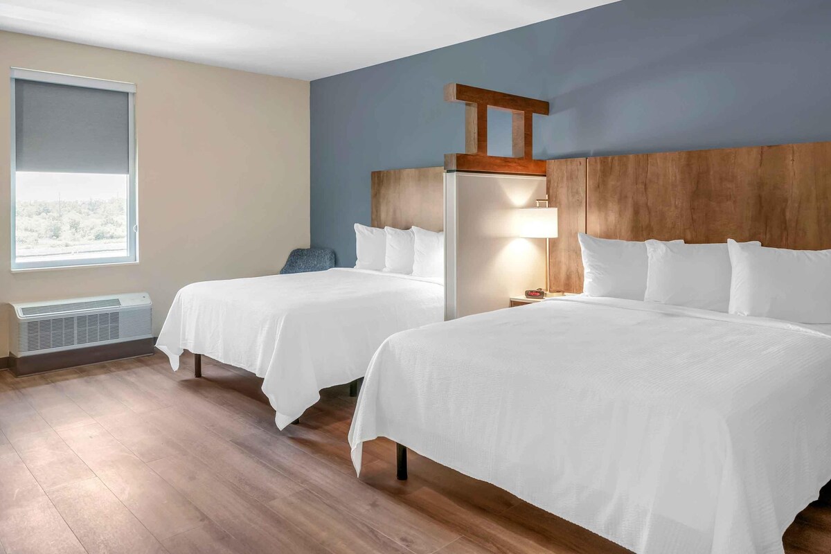 A hotel room with two beds, a heater, a window with a view, and a wooden headboard.