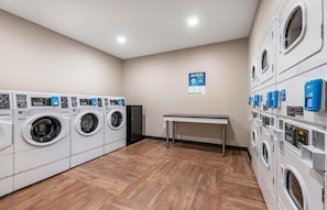 A laundry facility with multiple washing machines and dryers, a table, and a sign promoting an app.