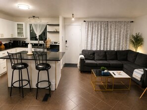Eine moderne Küche mit einer zentralen Kochinsel, Barhocker und einem dunkelgrauen Sofa in einem Wohnbereich mit Couchtisch.