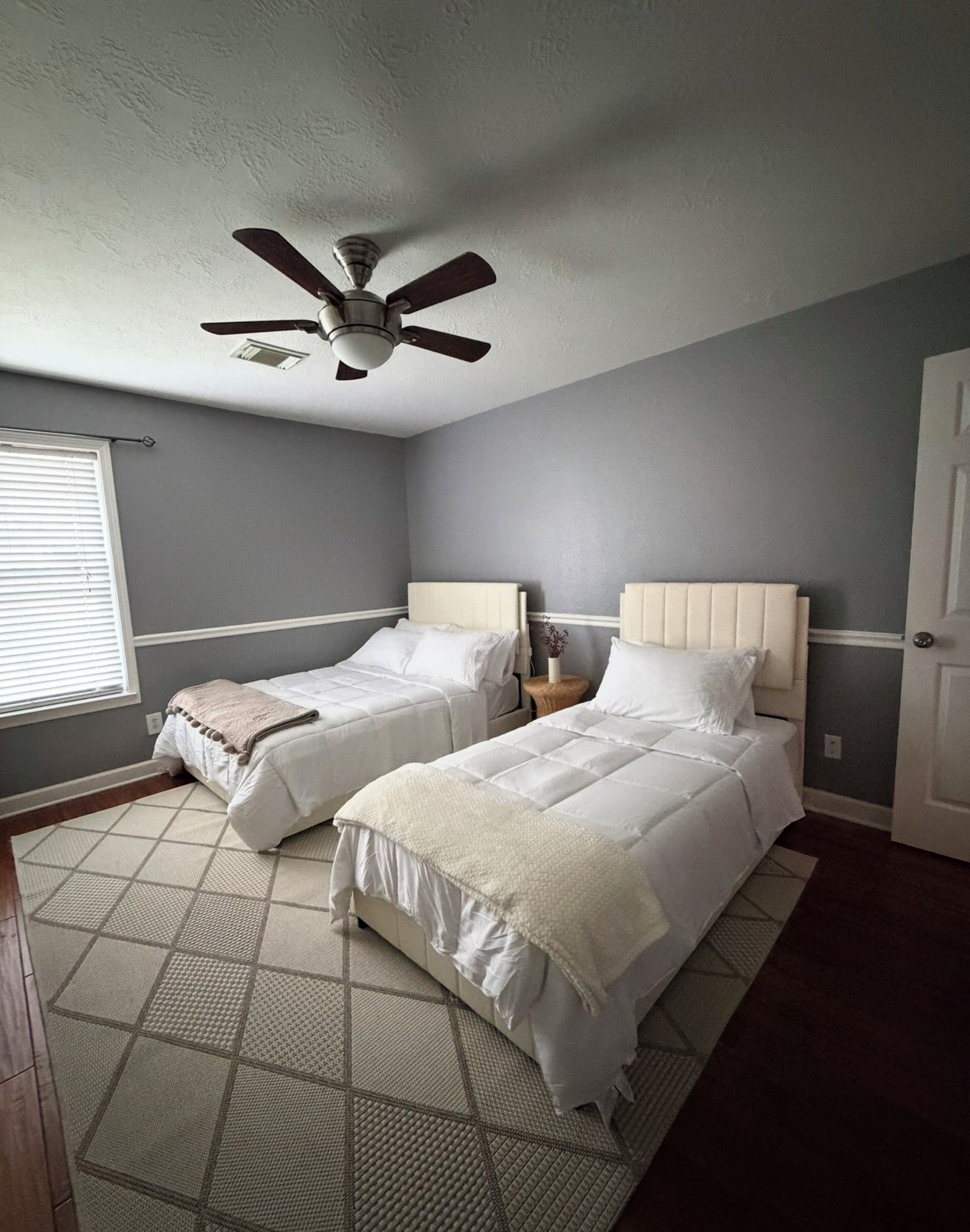 A bedroom with two beds, a ceiling fan, and a window with blinds.