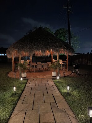 An outdoor patio area with a thatched-roof structure, seating, and a grill. - Your home away from home at Casa Palapa (Missouri City)