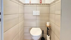 A small bathroom with a toilet, a hand dryer, and a toilet paper holder. - 'Le Belle Vue' Apartment: Mountain View, Shared Garden & Wi-Fi (Villard-de-Lans)