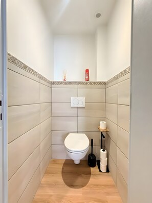 Um banheiro pequeno com vaso sanitário, secador de mãos e porta-papel higiênico.
