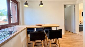 A modern kitchen with a wooden countertop, two pendant lights, and a dining area with a wooden table and black chairs. - 'Le Belle Vue' Apartment: Mountain View, Shared Garden & Wi-Fi (Villard-de-Lans)