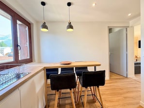Cozinha moderna com bancada de madeira, duas luminárias pendentes e área de jantar com mesa de madeira e cadeiras pretas.