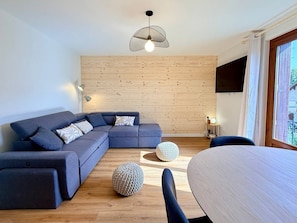 Una sala de estar moderna con un sofá modular, otomanas redondas, una mesa de comedor y una pared de madera.