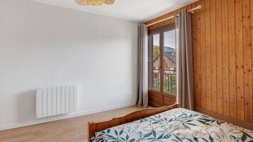 Un dormitorio con cama, radiador, pared de madera, ventana con cortinas y lámpara colgante.