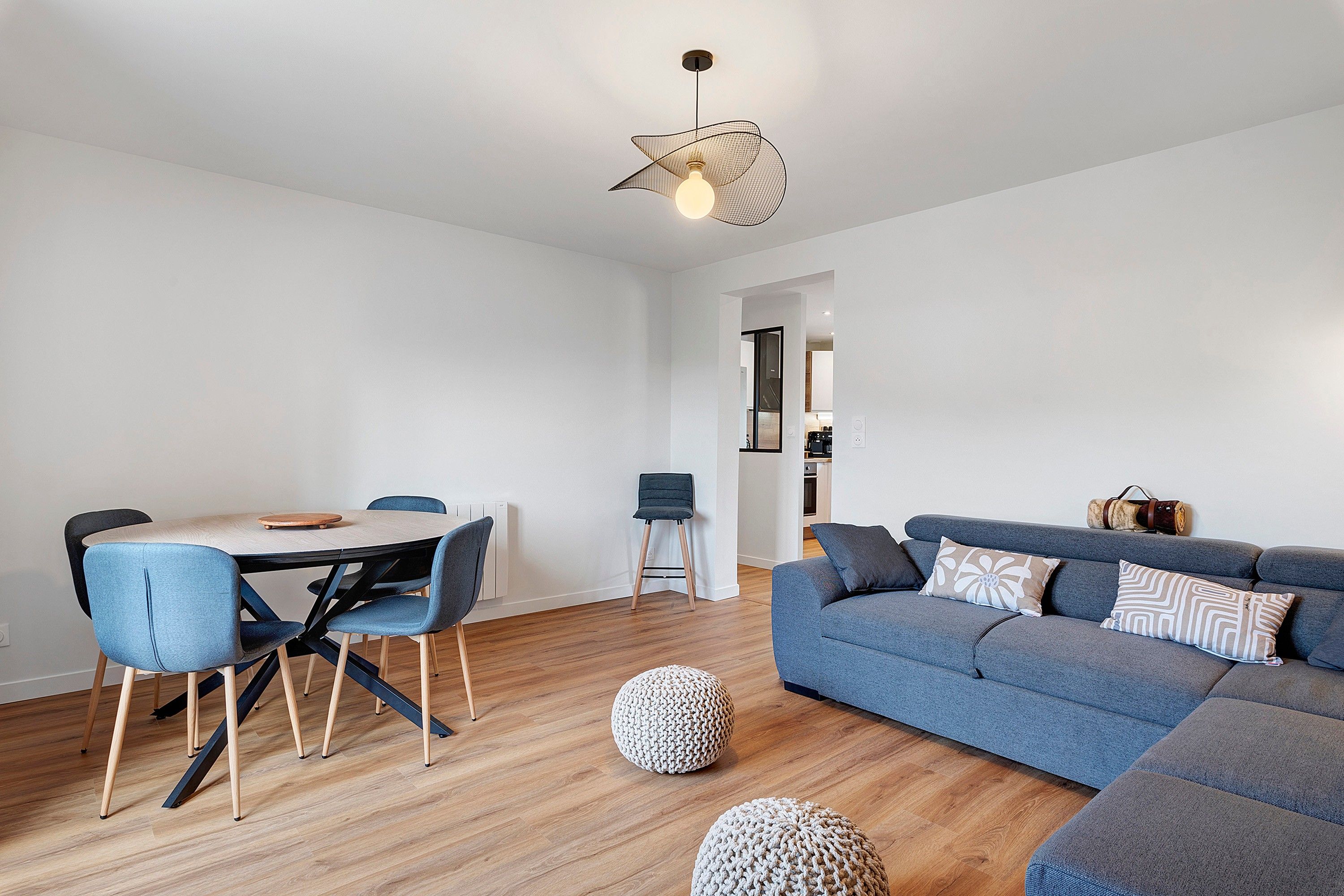 Een moderne woonkamer met een blauwe bank, een eettafel met stoelen en een bijzondere hanglamp.