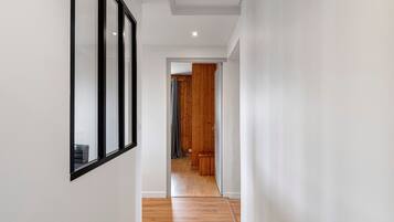 Un pasillo con piso de madera, paredes blancas y una puerta que da a otra habitación.