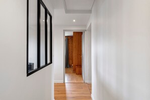 Een gang met houten vloer, witte muren en een deur naar een andere kamer.