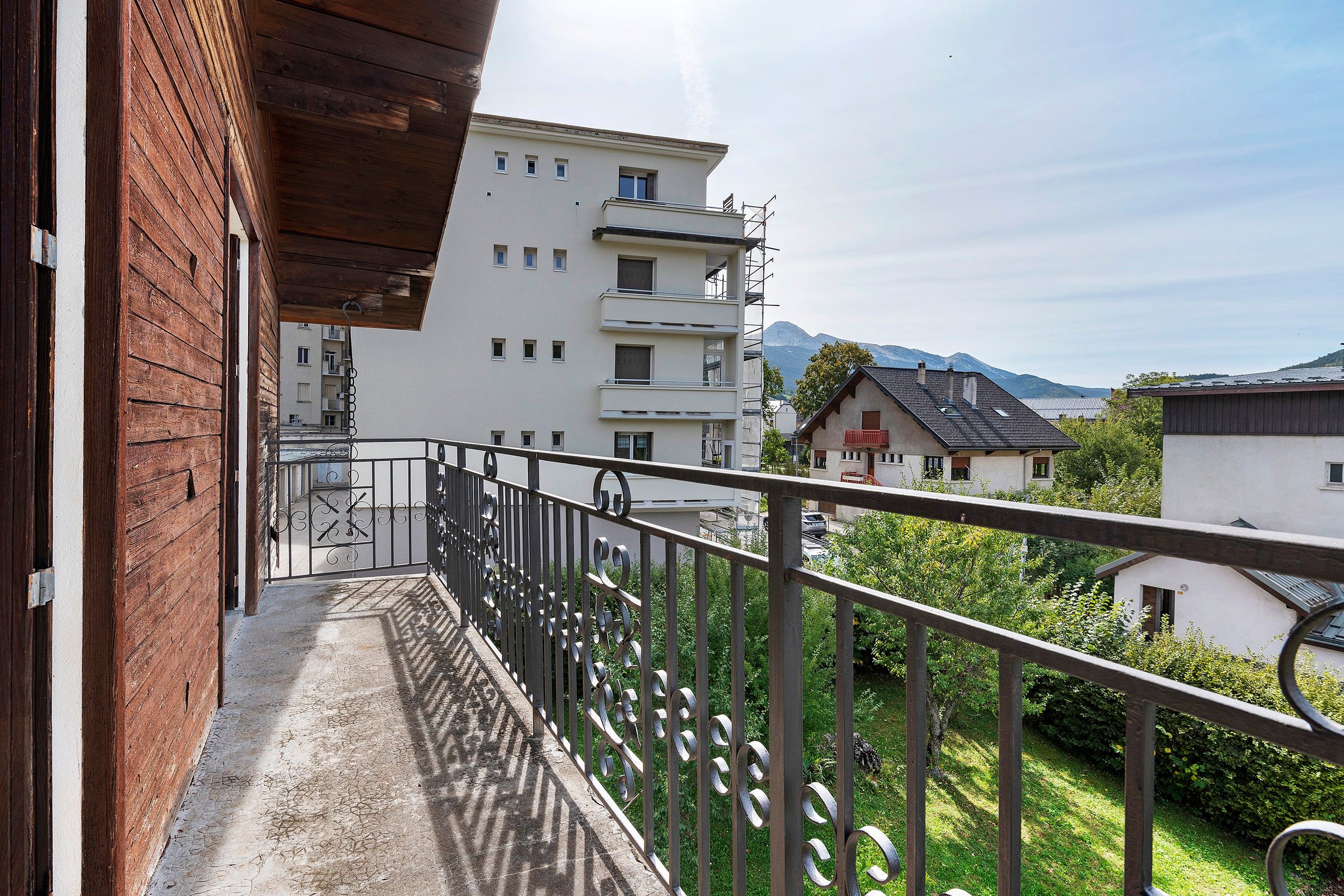 A balcony with a metal railing overlooking a residential area with houses and mountains in the background.