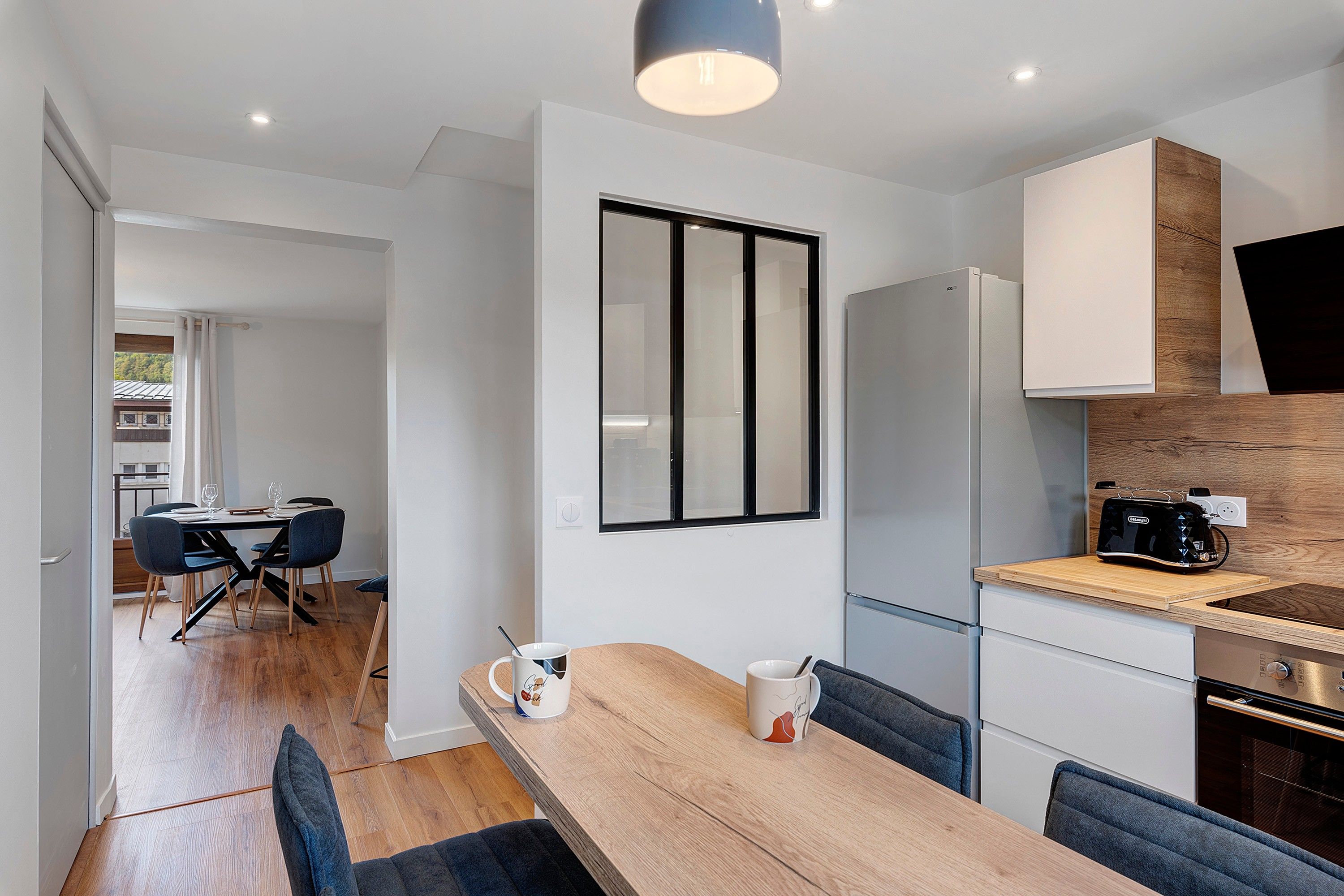 Una cocina moderna con una mesa de comedor de madera, sillas, un refrigerador y una cafetera.