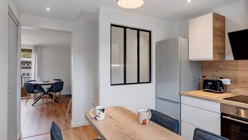 Una cocina moderna con una mesa de comedor de madera, sillas, un refrigerador y una cafetera.