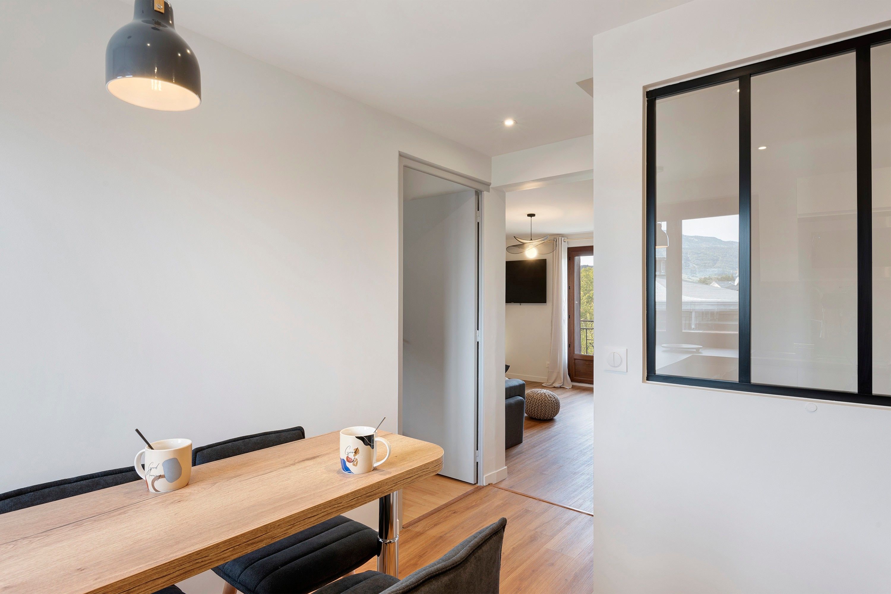Een moderne eethoek met een houten tafel, twee stoelen en een hanglamp.