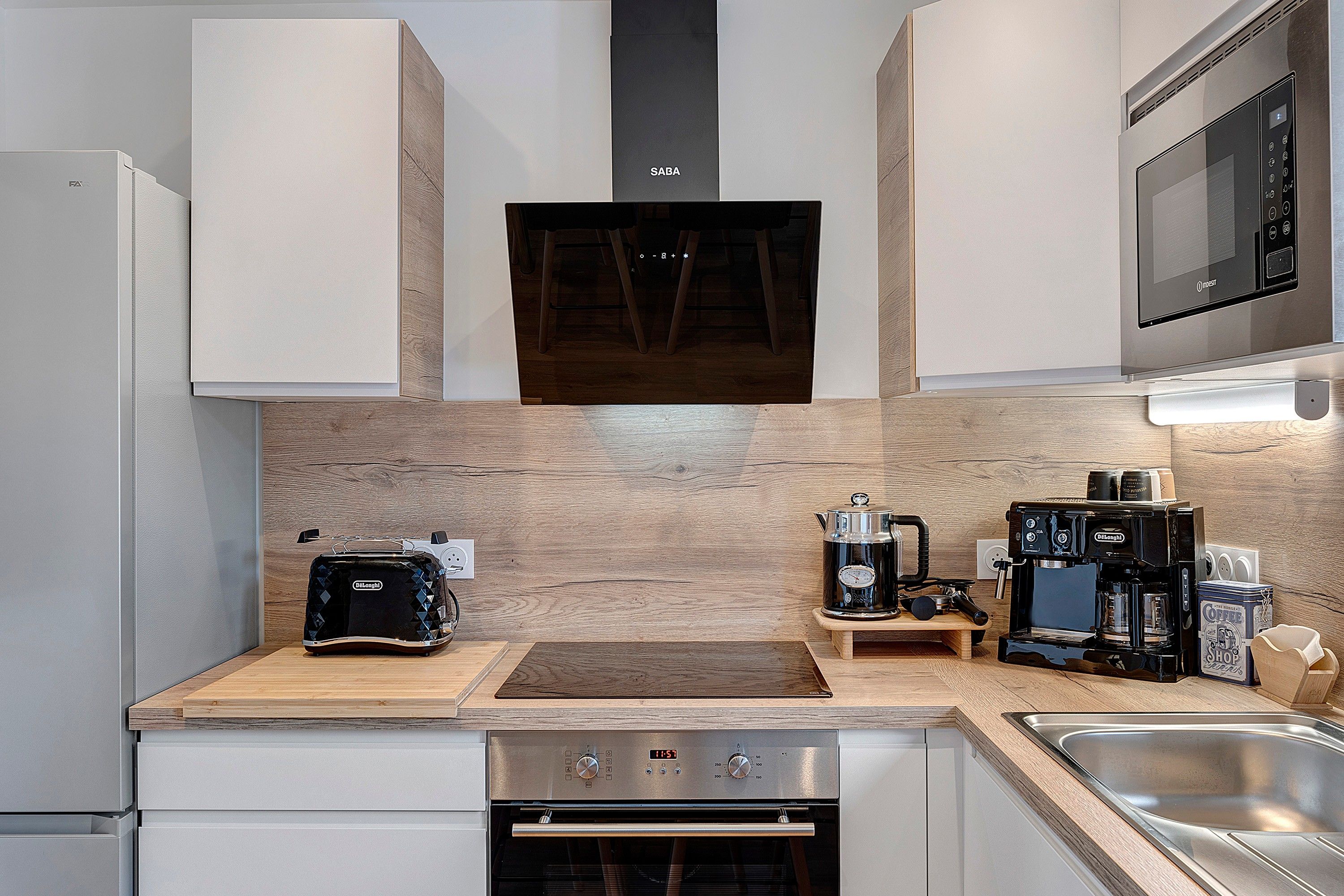 Een moderne keuken met een ingebouwde oven, een koffieapparaat en een magnetron.