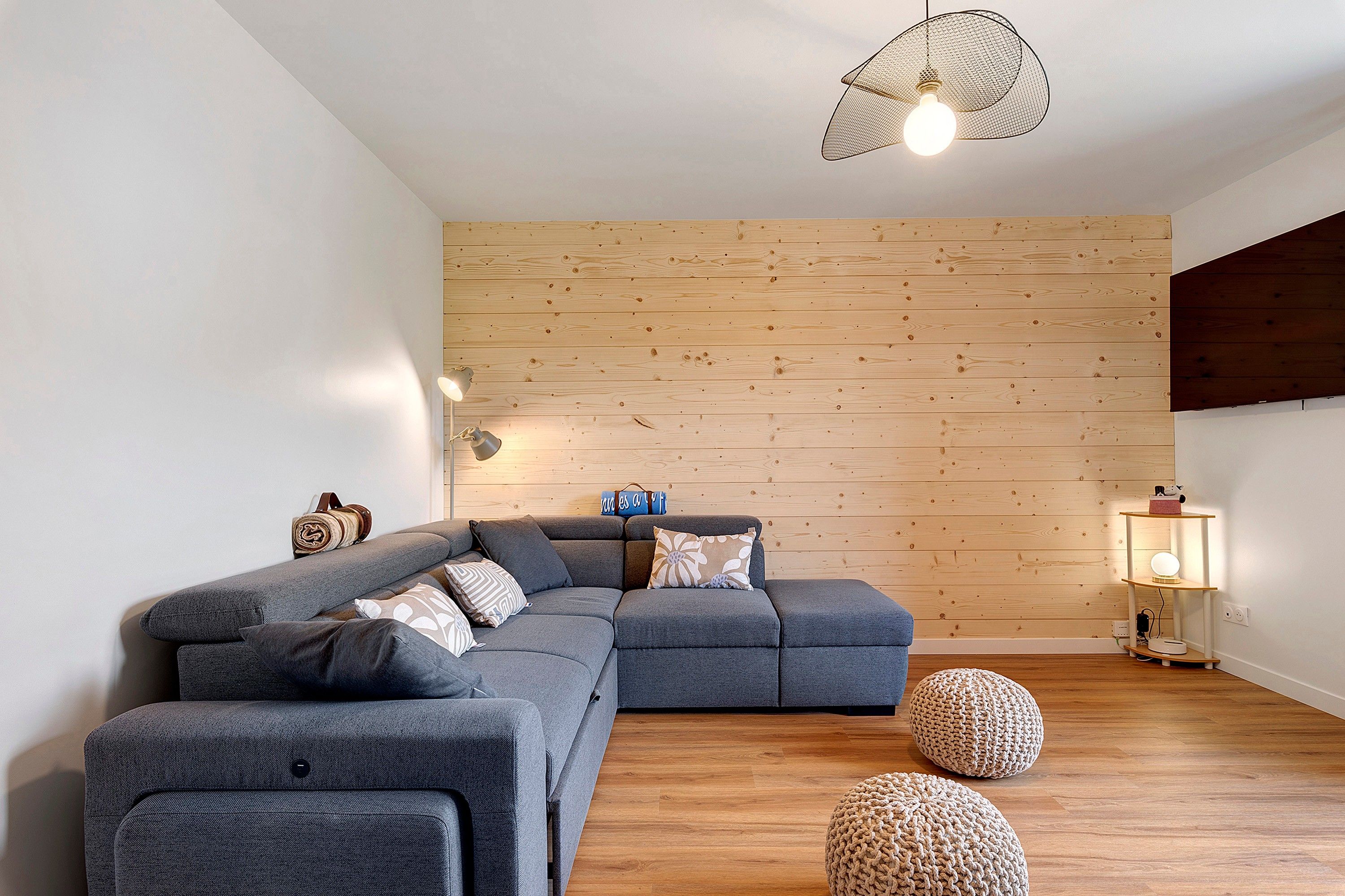 Een moderne woonkamer met een modulaire bank, een houten wand en een vloerlamp.
