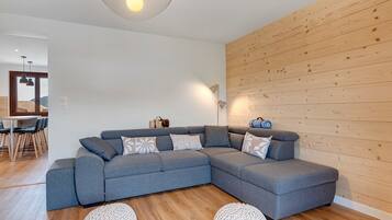 A modern living room with a grey sectional sofa, wooden wall paneling, a round knitted rug, and a pendant light.
