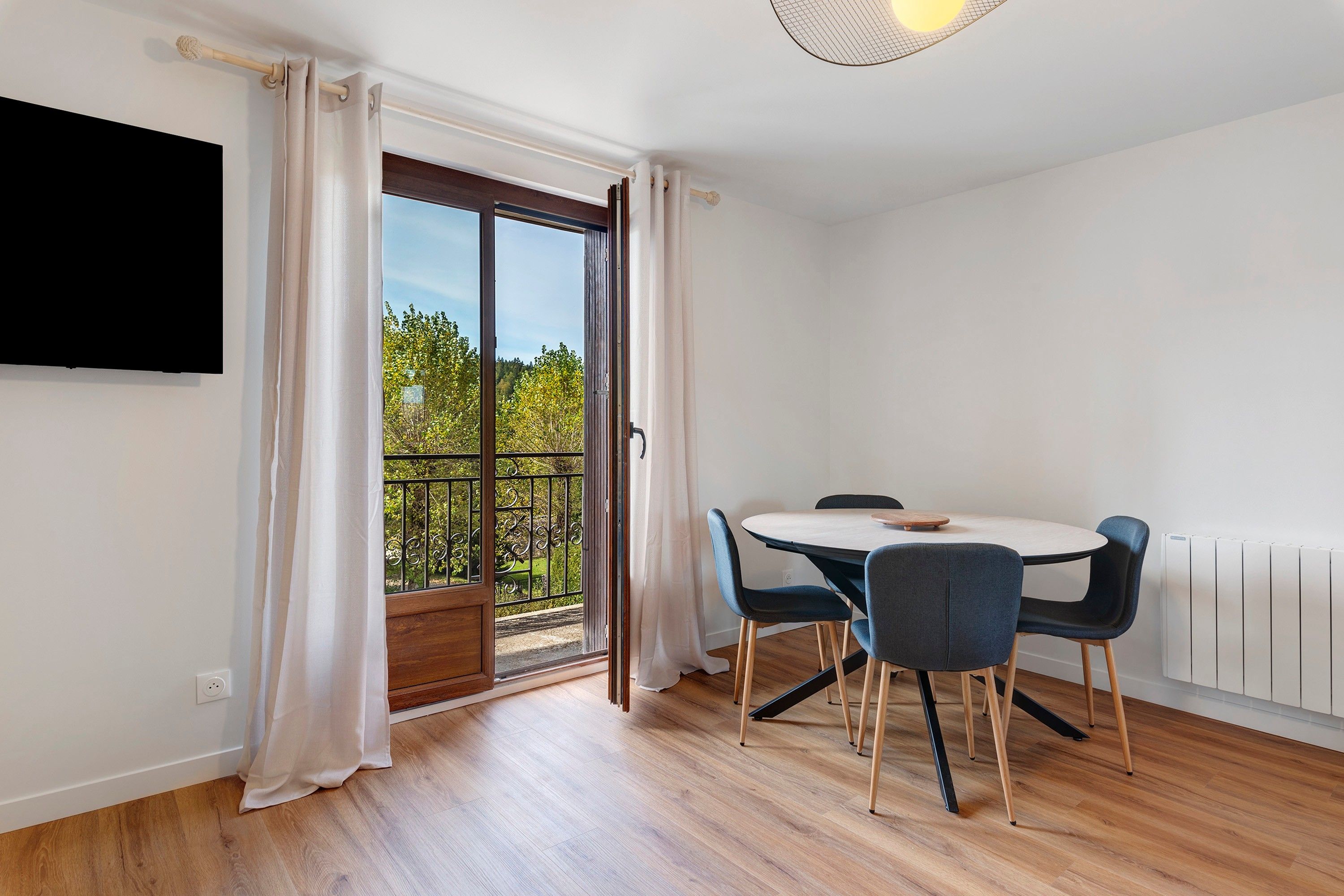 A room with a dining table, chairs, a TV mounted on the wall, and a sliding glass door leading to an outdoor area.