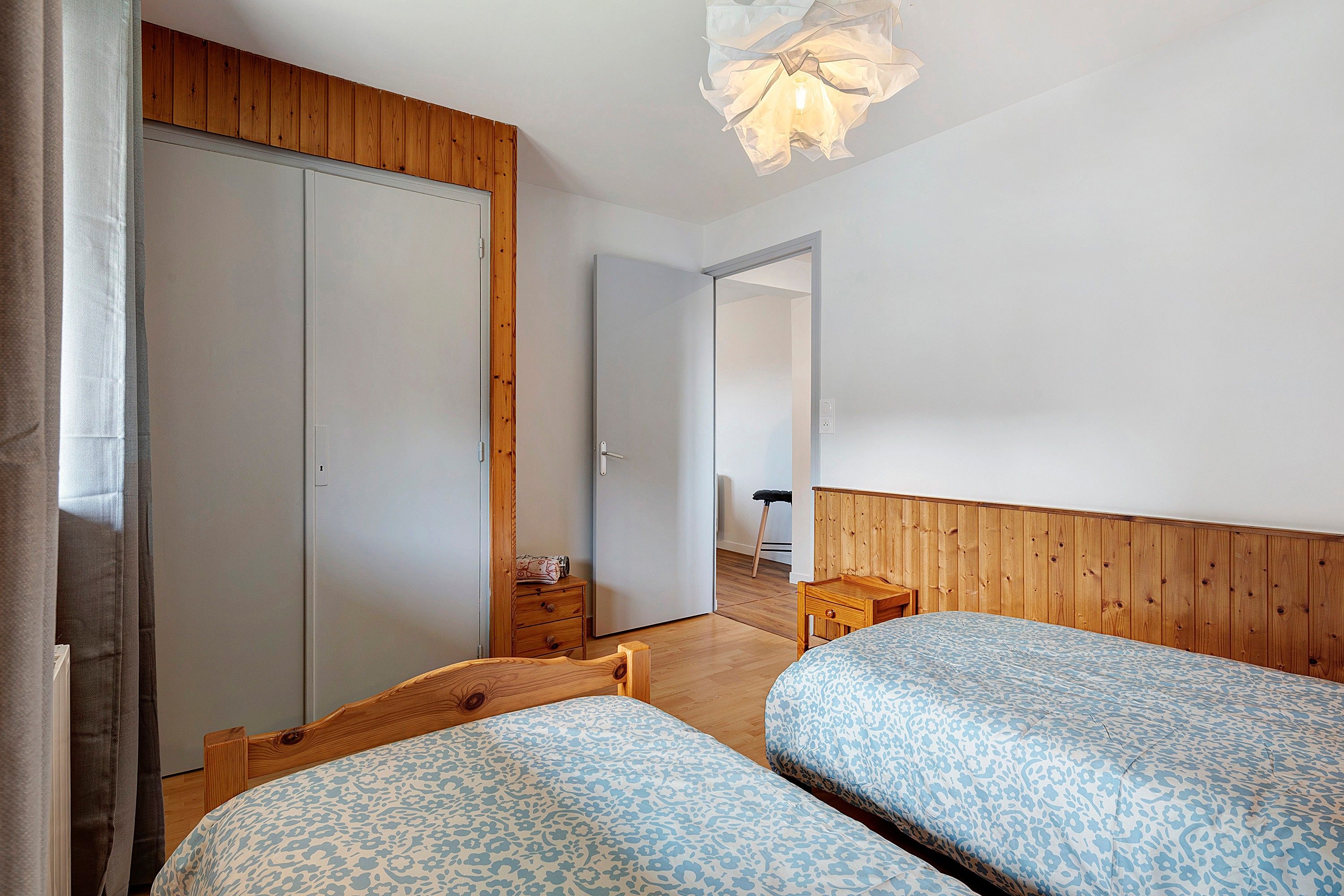 Een kamer met twee houten bedden, een houten kledingkast, een klein houten tafeltje en een lamp.