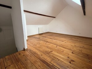 Une pièce vide avec un plancher en bois, un radiateur et un plafond en pente.